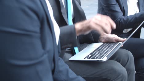 primer plano de un hombre de negocios irreconocible con computadora portátil sentado cerca de socios o colegas afuera y hablando