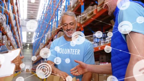 Animation-of-network-of-digital-icons-over-two-caucasian-male-volunteers-shaking-hands-at-warehouse