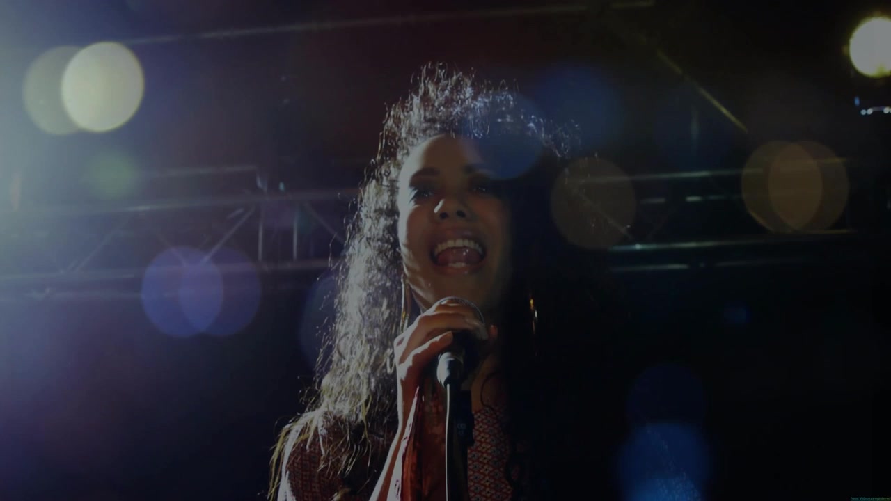 Singer starting singing into mic under lights, whipping hair, lens flares, energizing concert fans