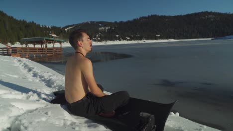 man sitting on yoga mat beside frozen lake