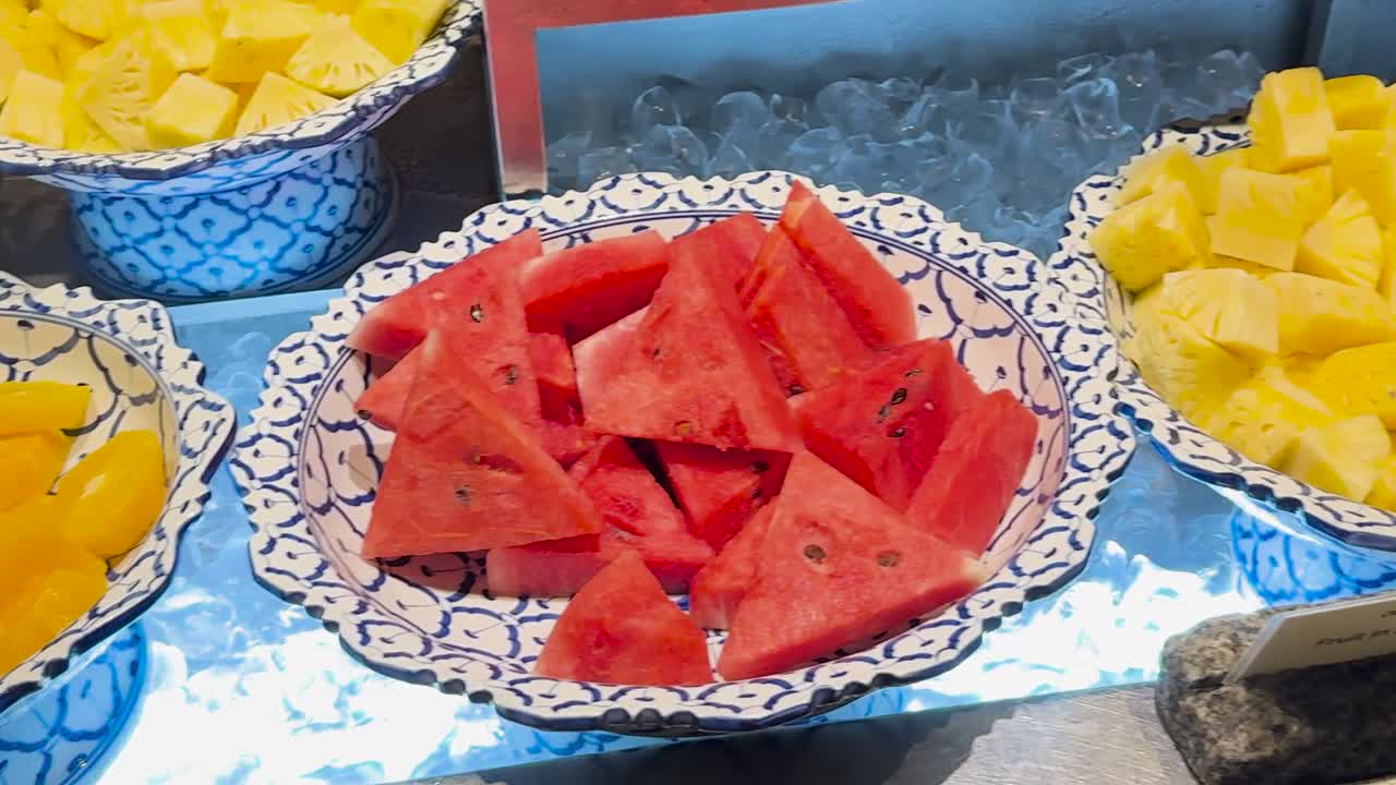 A colorful arrangement of watermelon, pineapple, and papaya slices on patterned plates, showcasing a fresh fruit selection.