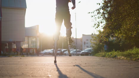 back shot of guy wearing gray hoodie and dark gray pants jumping on spring stilts on paved road in residential area surrounded by houses during sunset, showcasing dynamic motion