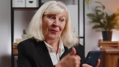 surprised senior woman using smartphone typing browsing celebrating success victory at home office