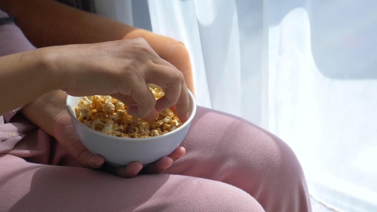 mujer disfrutando de palomitas de maíz junto a la ventana