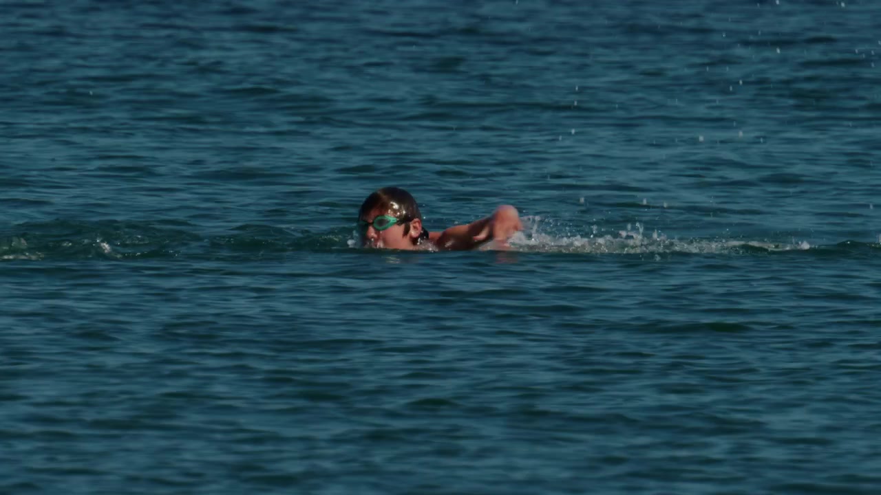 紺碧の海で水しぶきを上げながら自由形で泳ぐスイマー。フィットネス、トレーニング、夏のレジャーを表現しています。