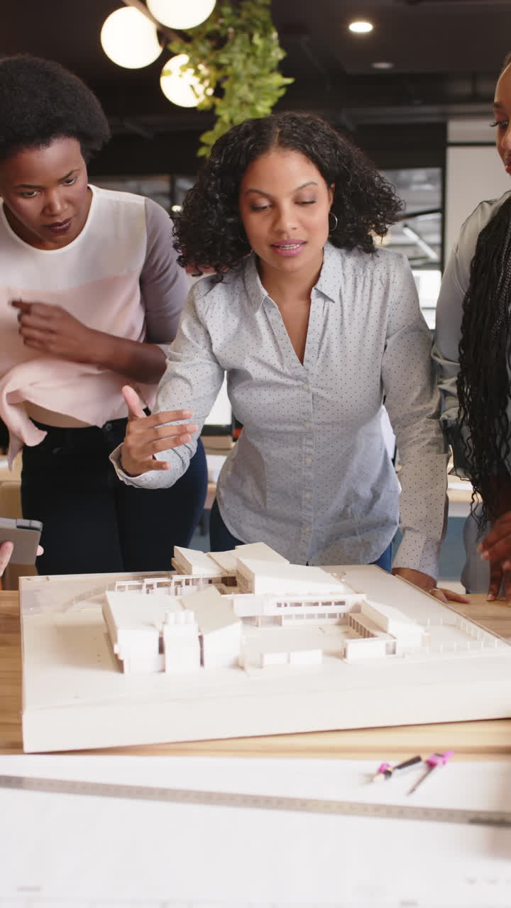 Vertical video of busy diverse businesswomen discussing building model in office in slow motion
