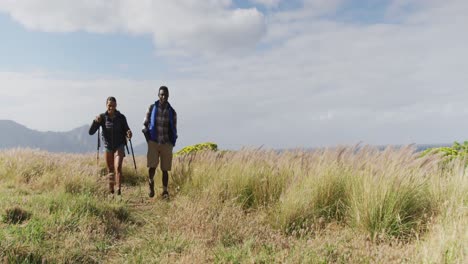 pareja diversa con mochilas usando palos de senderismo nórdicos caminando en el campo