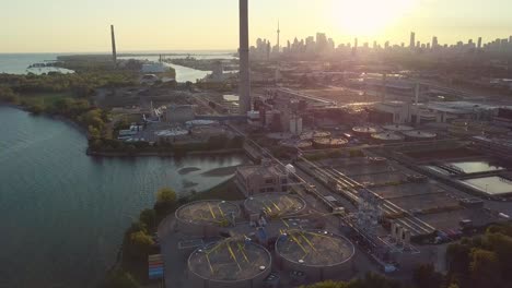 aerial sunset wide shot sliding left over lake shoreline showing industrial factory and huge smokestack tower with downtown skyline in background in toronto ontario canada