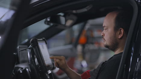 mechanic uses a tablet computer with an augmented reality diagnostics software. specialist inspecting the car in order to find broken components inside. male uses laptop for diagnostics vehicle