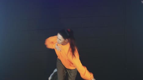 attractive young female in orange blouse dancing modern freestyle hip hop dance in a studio