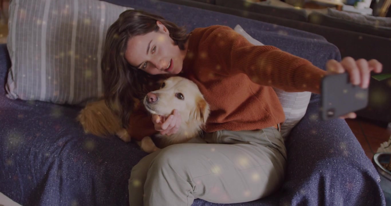 Donna che coccola un retriever su un divano blu e che estende lo smartphone, scattando un selfie per i social media.