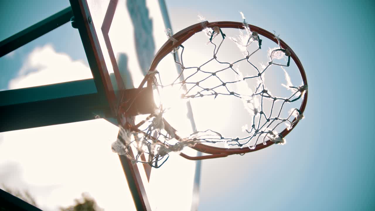 un aro de baloncesto, la red revoloteando en el viento, la luz del sol brillante.