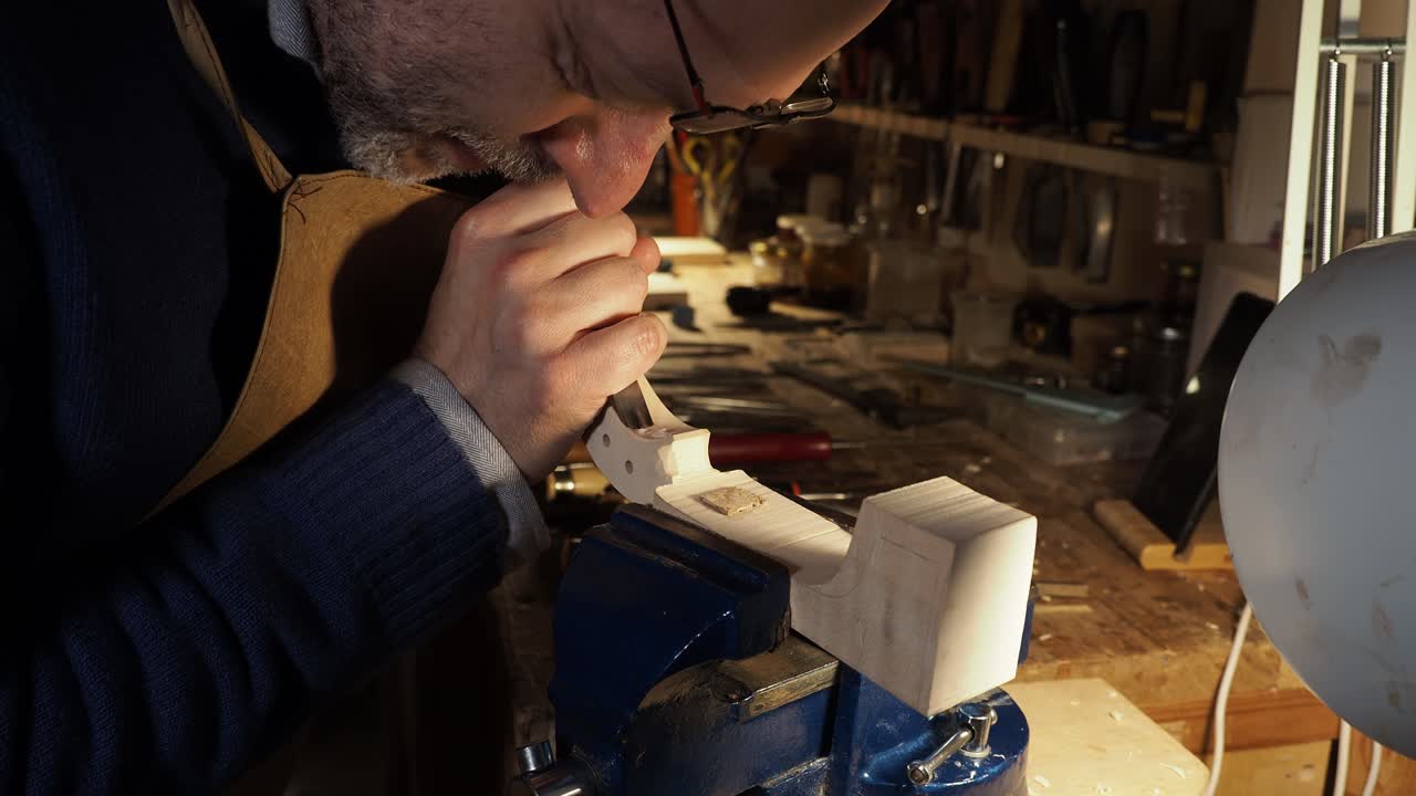 Close-up of artisan carvinga violin scroll wood at workbench, focus on skilled hands, precise craft and manual detail in workshop