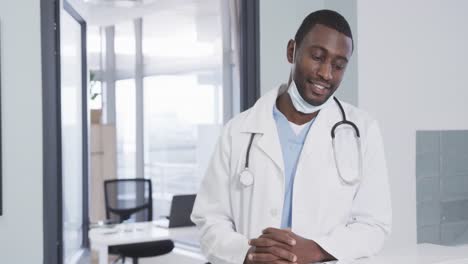 portrait of happy african american male doctor with face mask in hospital, slow motion