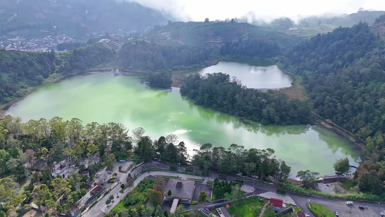 Drone view of a calm mountain lake reflecting the surrounding forest and foggy hills. Peaceful and breathtaking highland environment. Telaga Warna, Dieng, Indonesia