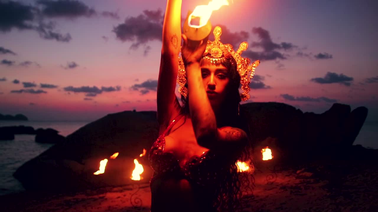 Erotic and sensual belly dancer, performing sexy moves with fire palm torch props, on the beach during golden hour. Close up.
