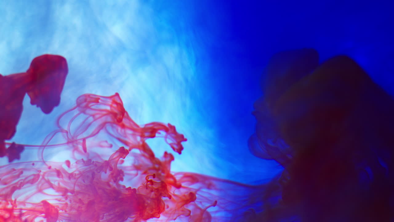 Red And Blue Paint Or Dye Dropped Into Water Against White Background To Create Swirling Colourful Smoke Background