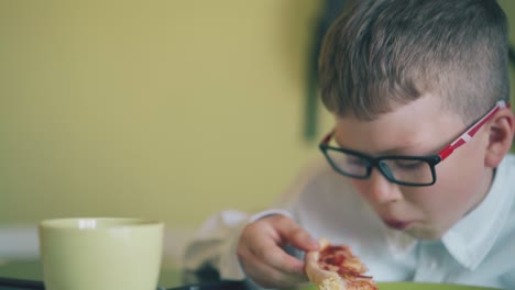 pupil-eats-slice-of-fresh-pizza-at-cup-on-table-in-canteen