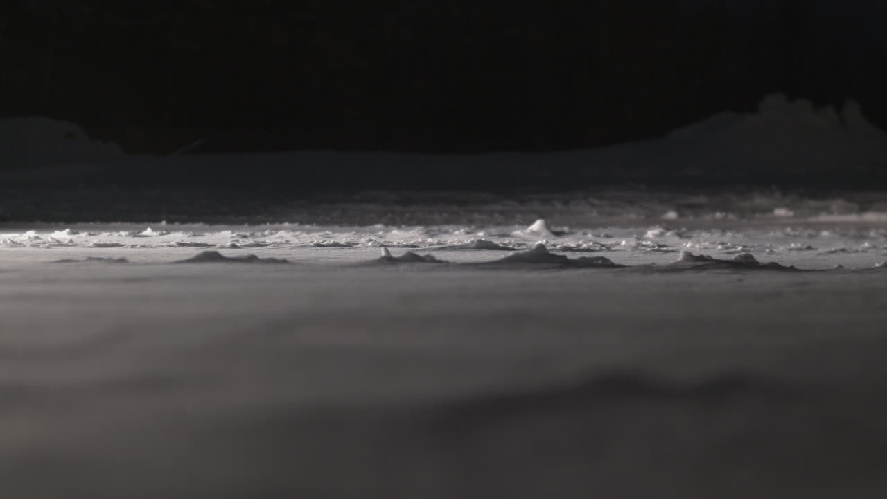 крупный план снега, летящего по замерзшей земле в темноте