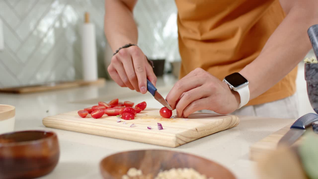 Home cook's hands are reaching and slicing tomatoes for salad on wooden cutting board