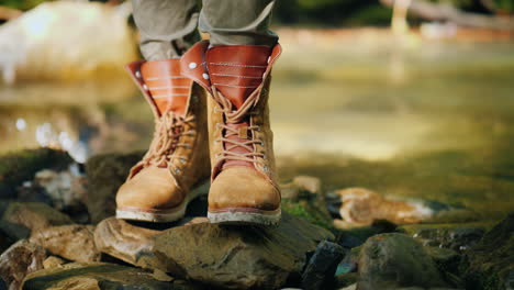 a tourist in trekking boots stands near a mountain stream hiking and active rest