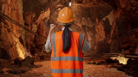 back view of a female engineer with safety helmet raising her hands celebrating while working in underground mine tunnel