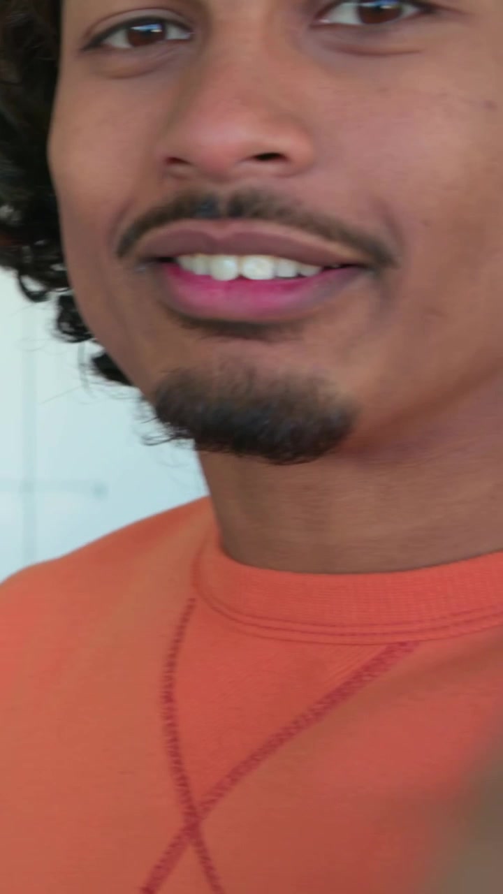 Vertical video: Pressing record orange shirt man moving closer and back in kitchen filming on phone