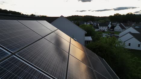 Solar panels on roof of single family house. Aerial close up shot. Sunset time in modern american neighborhood. Sun reflection on units of photovoltaic array.