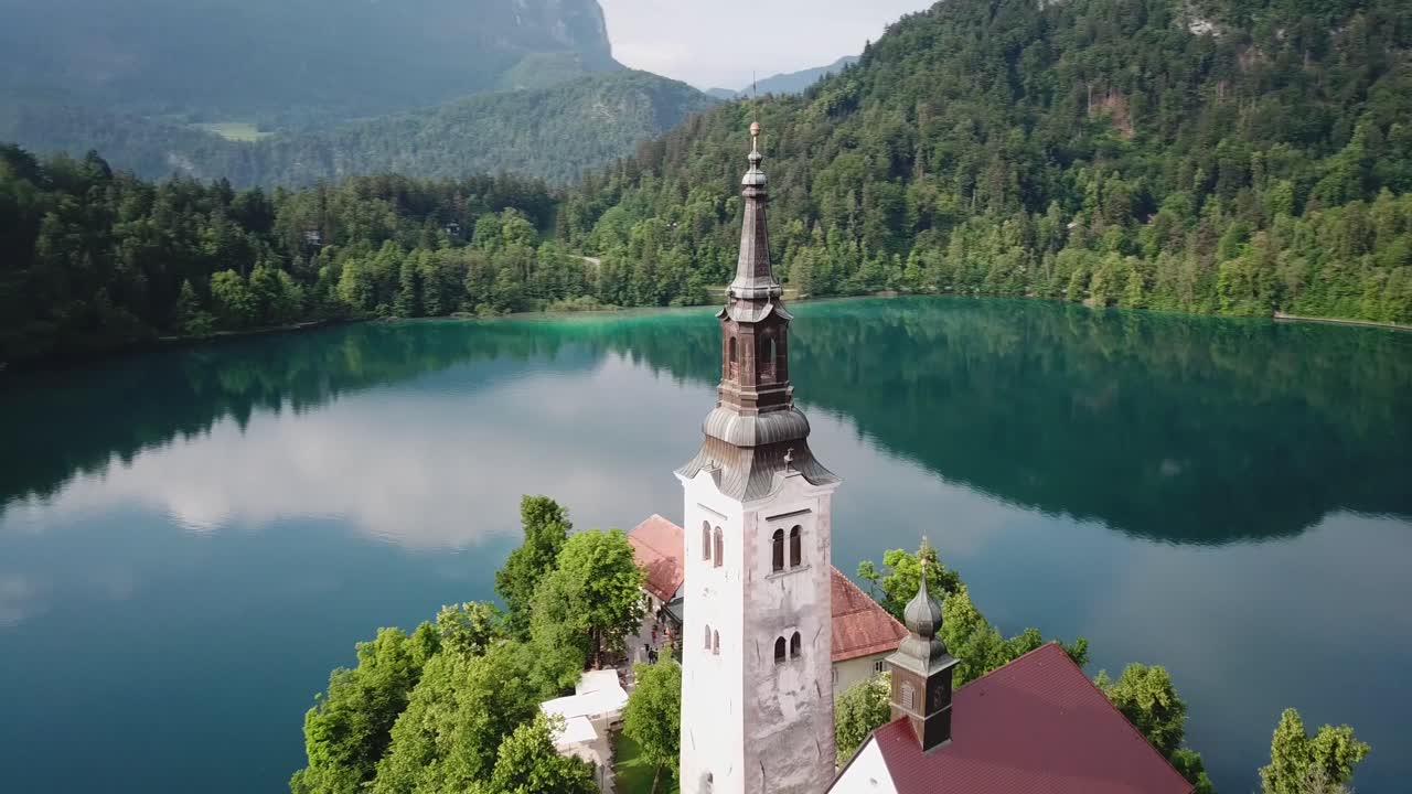 Veduta aerea orbitante di un campanile di chiesa circondato dalle acque limpide del Lago di Bled in Slovenia.