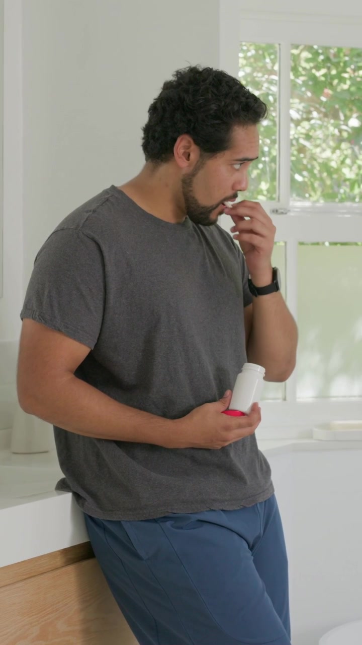 Vertical video: Opening pill bottle red cap, man at sink pouring pills, checking watch, taking meds