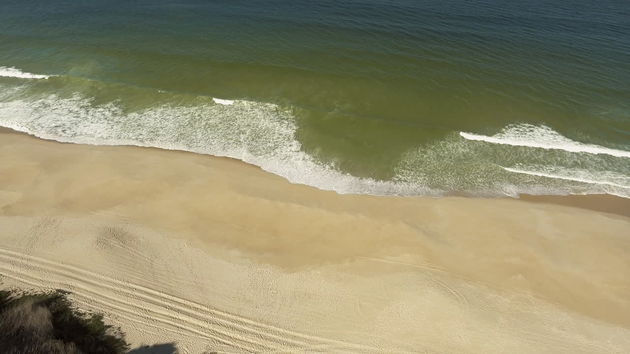 밝고 화창한 날 포르투갈의 프라이아 다 게일 캠핑 근처에서 강풍의 모래 해안에 파도가 튀는 모습 - 공중 드론 촬영