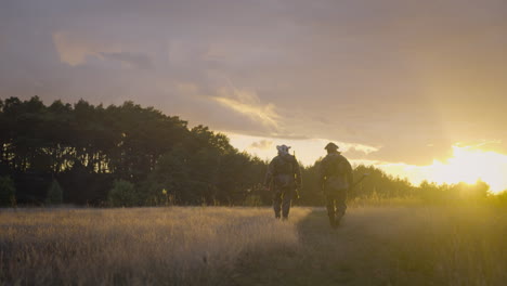 hunters walking through a field at sunset
