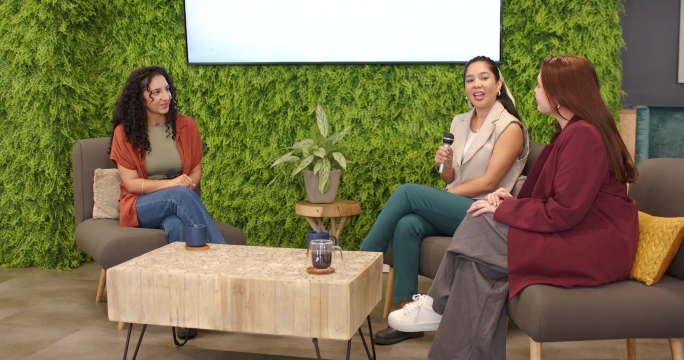 Female panelists prompted by Let's Talk About AI slide exchanging mics, sharing AI ideas in lounge
