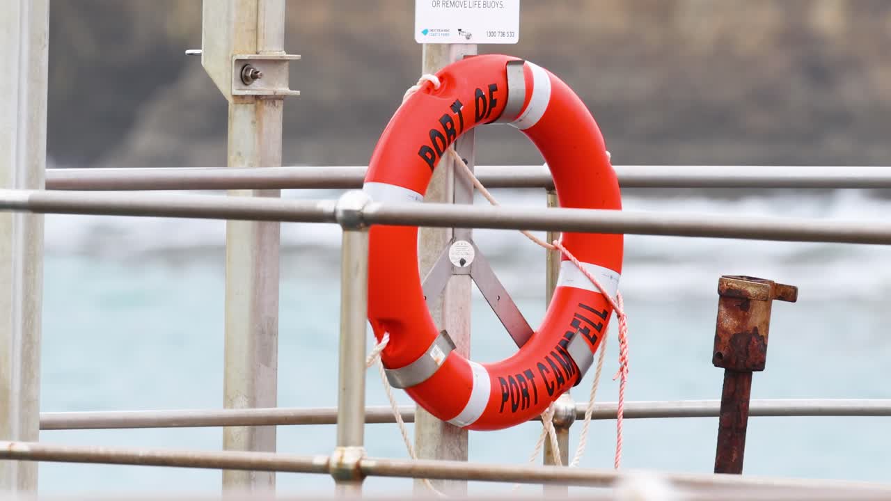 A bright orange lifebuoy attached to a metal railing with a calm ocean in the background.