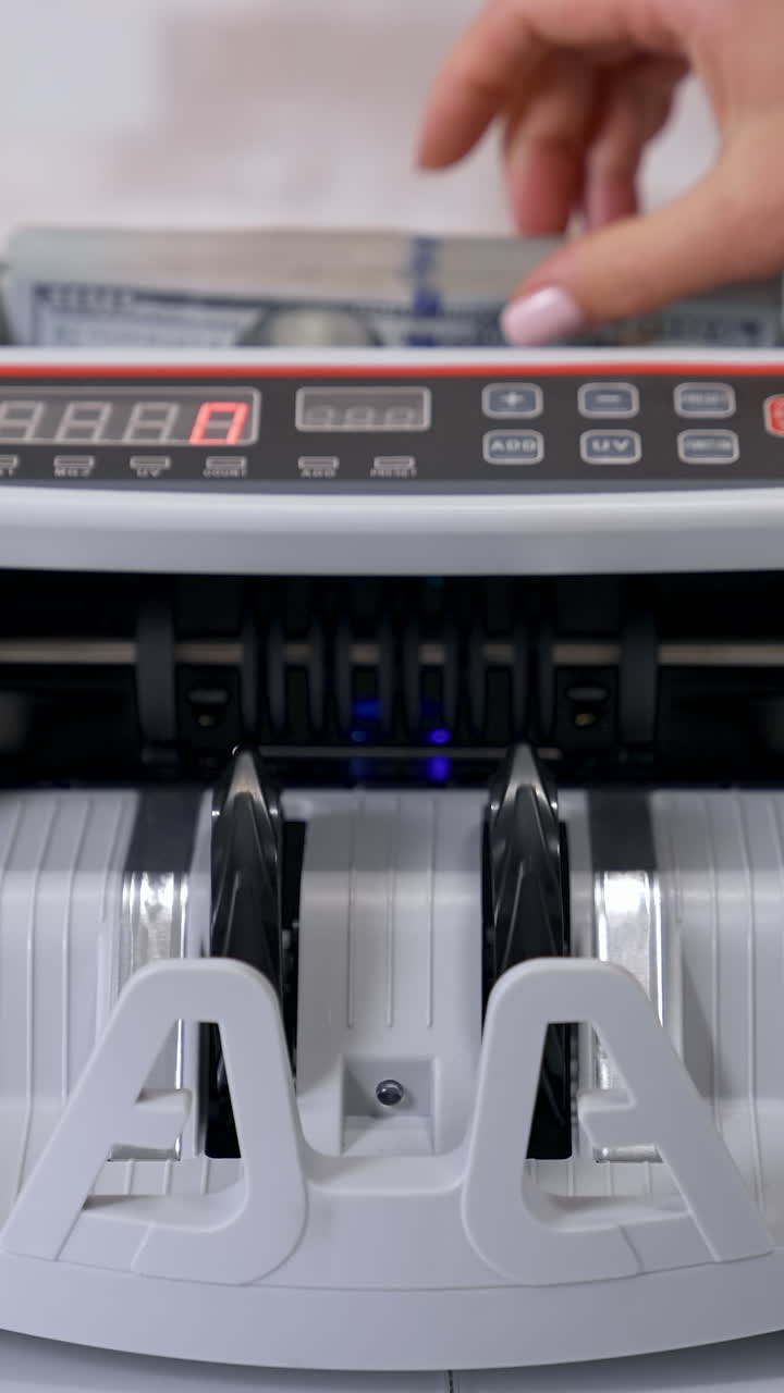 Equipment for counting money. Wad of hundred dollars are counted in a calculating machine. Automatic equipment for banking financial transactions. Female's hand puts money into electronic machine. Vertical video