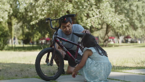 Neugierige-Kleine-Tochter,-Die-Mit-Ihrem-Vater-Das-Pedal-Ihres-Fahrrads-Im-Park-Dreht