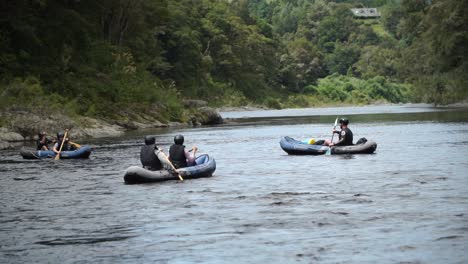 SLOWMO---Group-of-kayakers-going-down-the-beautiful-blue-pristine-clear-Pelorus-river,-New-Zealand-with-native-lush-forrest-in-background