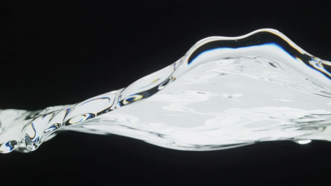 Flowing clear liquid ribbon moving left to right in studio, tension shaping teardrop highlights