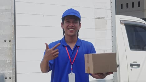 young asian delivery man holding cardboard box package and showing thumb up with happy smiling expression