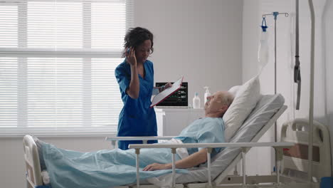 An-elderly-white-man-of-60-70-years-old-is-lying-in-a-hospital-bed-talking-to-a-black-woman-doctor.-Discussion-of-treatment-with-a-cardiologist-neurologist.-Rehabilitation-plan-after-recovery