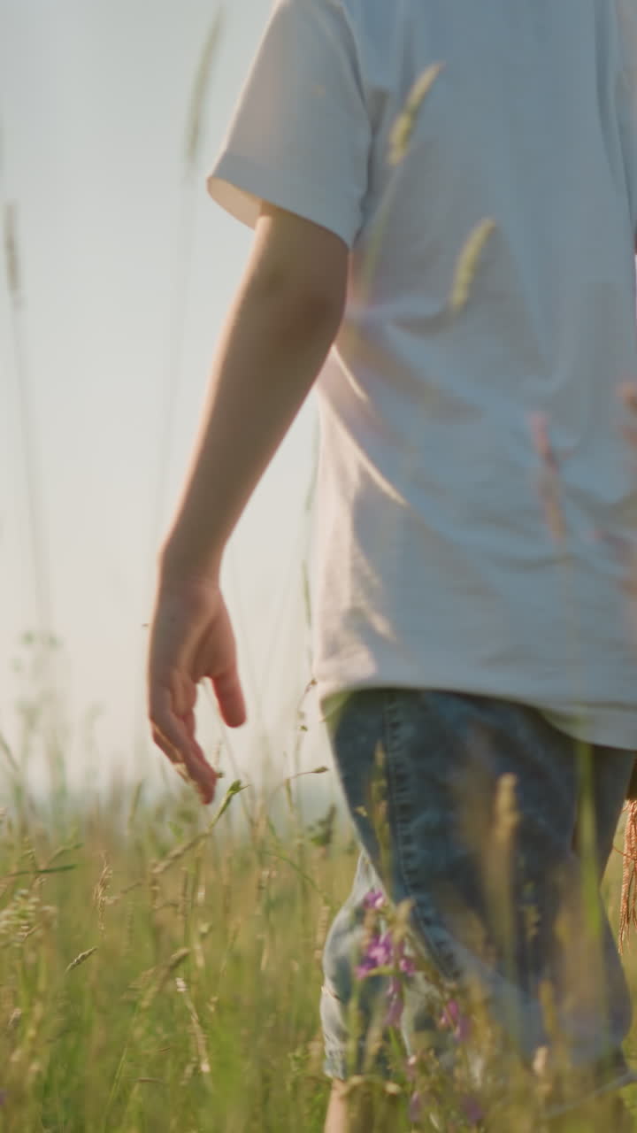 색 셔츠와 청바지를 입은 어린 소년의 하부 몸의 클로즈업, 과일 바구니를 들고 있는 파란색 드레스를 입은 여자와 함께 고, 그들은 빛으로 빛나는 잔디을 통해 함께 습니다.