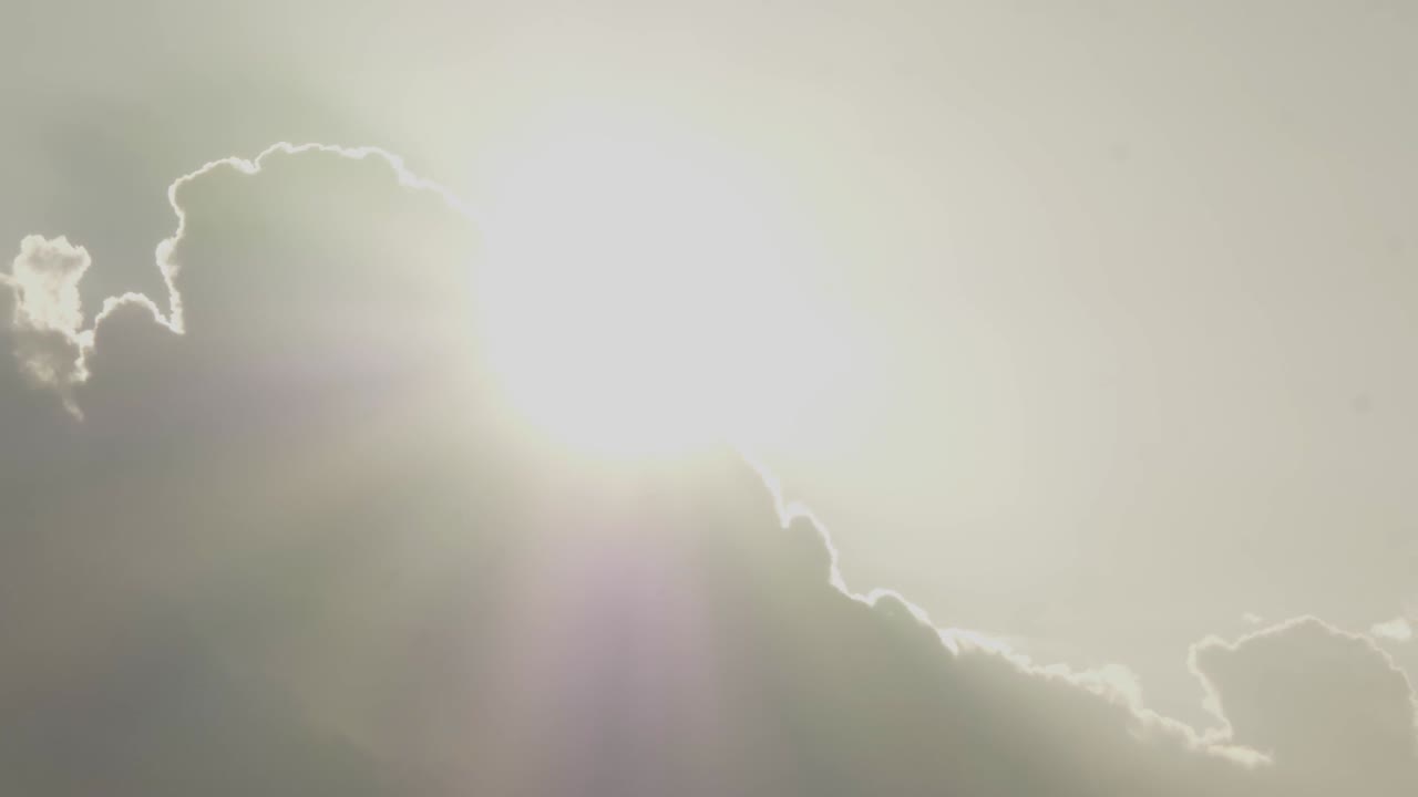 Bright sun emerges from behind clouds with light rays, heavenly sky, timelapse