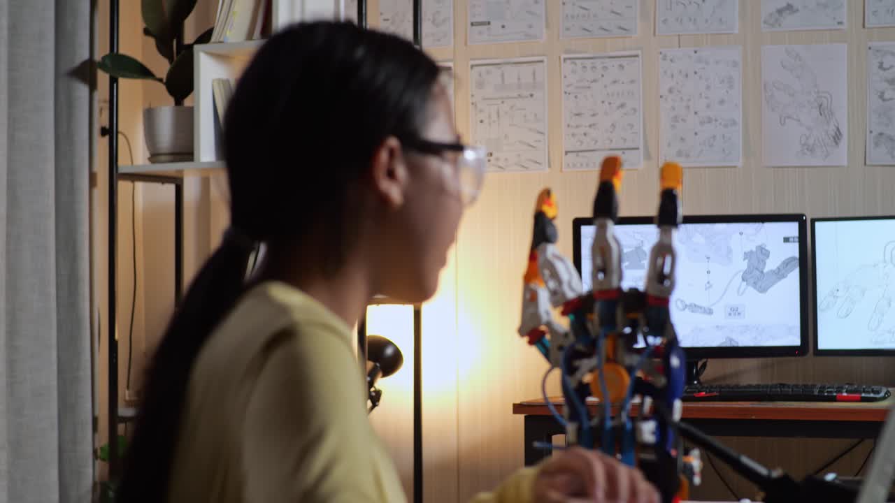 집에서 사이보그 손에 대해 작업하는 동안 벽에 있는 그림을 보려고 는 십대 아시아 소녀의 가까운 사진