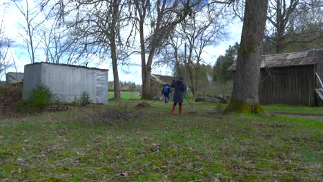 timelapse footage of young energetic people raking leaves in a rural countryside garden when sun is occasionally coming out behind the clouds and lighting the green meadows and leaves on the ground.