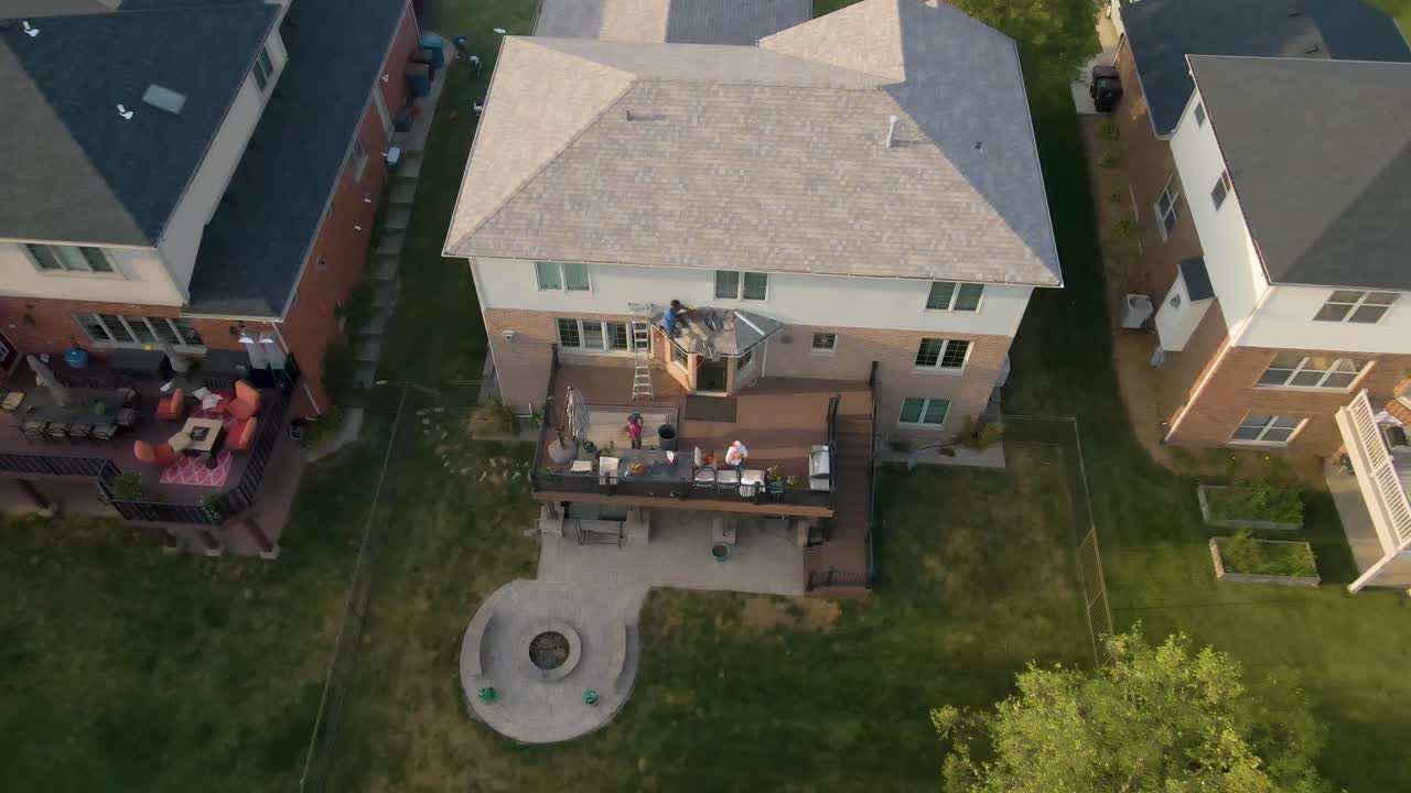 Aerial view of construction workers laboring in a backyard patio with outdoor furniture, a fire pit, and a well-maintained lawn, showcasing a cozy and inviting outdoor living space.