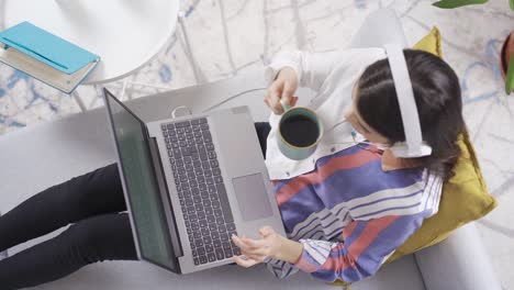 mujer joven feliz sentada en casa y usando una computadora portátil mientras bebe café. escucha música.
