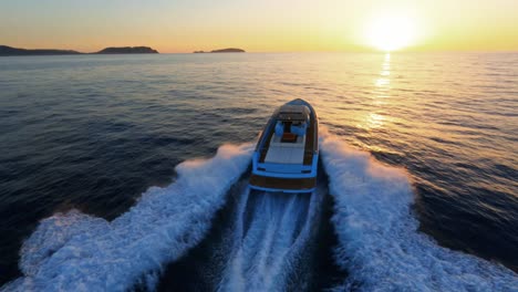 aerial drone view following a luxury yacht cruising toward the sun as it sets below the horizon.