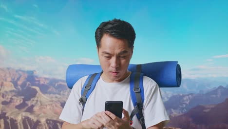 close up of asian male hiker with mountaineering backpack looking at the smartphone and saying wow while traveling at the top of mountain