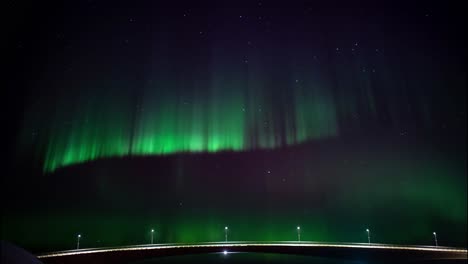 dancing aurora borealis at night time over a illuminated bridge in scandinavia