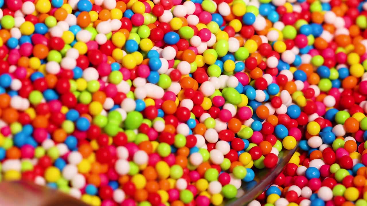 A spoon filled with vibrant, multicolored sprinkles in a detailed close-up view.